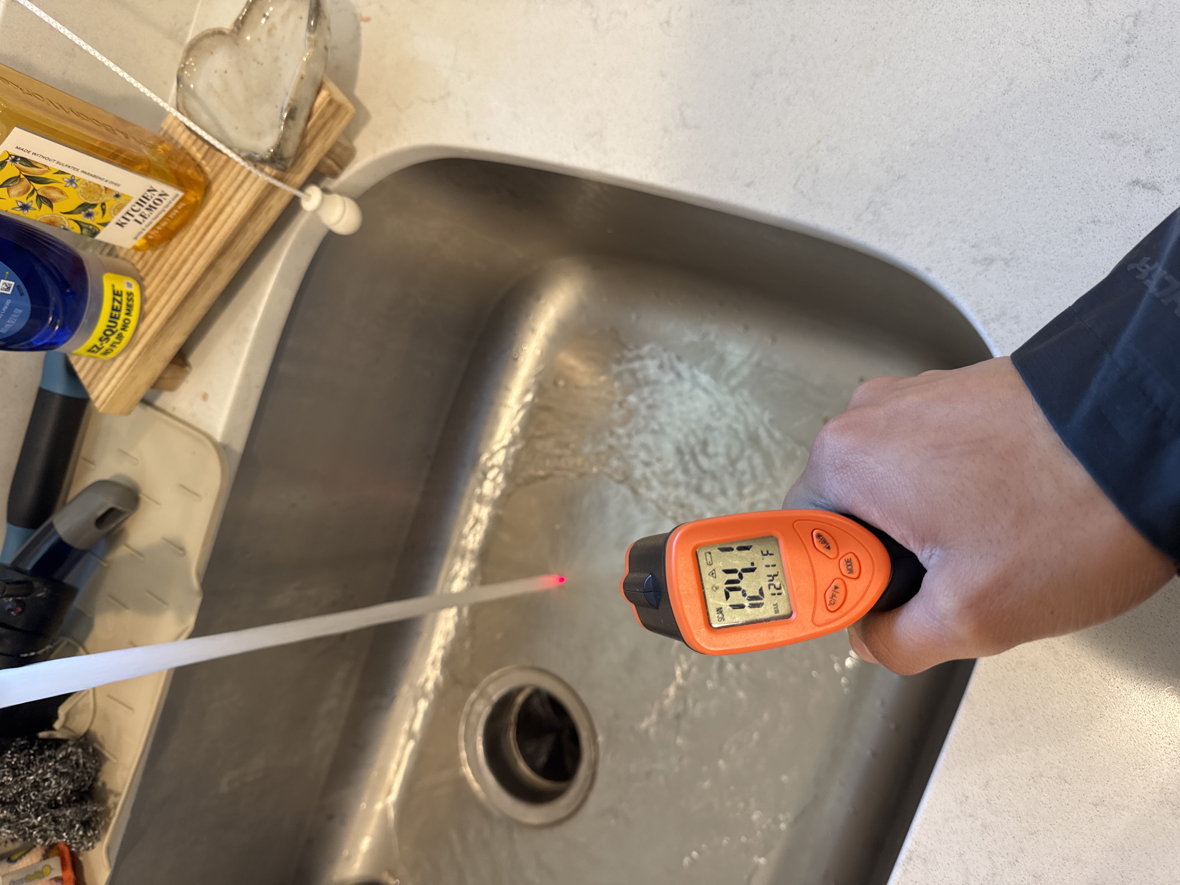 Infrared thermometer measuring hot water temperature at a kitchen sink